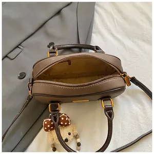 Brown retro bowling bag with plush bear charm and adjustable strap on office blazer