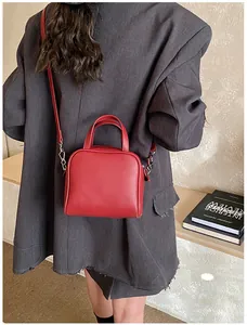 Model wearing a red mini square handbag over a grey suit to show the shoulder strap style
