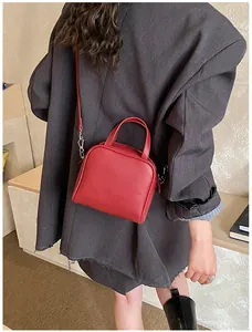 Detail of red matte leather handbag with adjustable strap worn by a model in a grey blazer