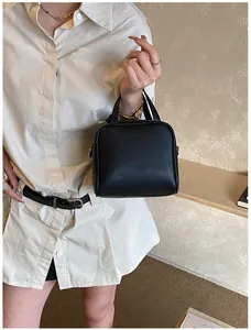 Detail of a minimalist black leather mini square handbag held by a model in soft light
