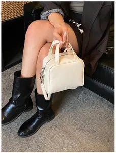 Detail view of cream square handbag with dual handles and side metal hook strap