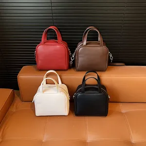 Minimalist square crossbody bags in red, brown, white and black on a leather sofa