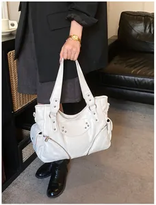 Détail d'un sac cabas en cuir blanc avec des rivets de style motard et des poches zippées