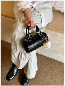 Detail of black cylindrical handbag with leather texture and white plush sheep charm