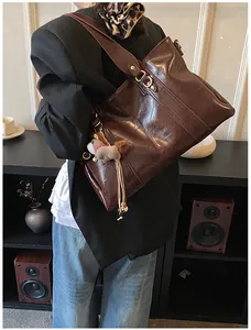 Detailansicht einer großen braunen Vintage-Tasche mit goldenen Ringen und Plüschbär-Anhänger