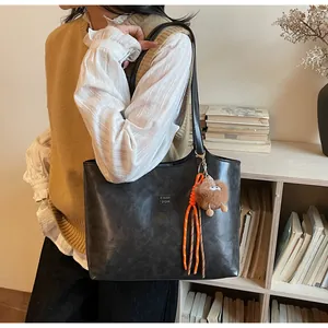 Détail du sac cabas noir avec texture rétro, lettrage doré et accessoire de pendentif