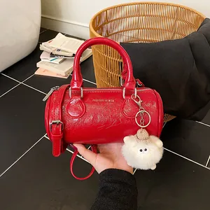 Red cylindrical boston handbag with plush charm and adjustable strap for women