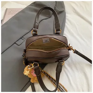 Minimalist dark brown leather Boston bag with plush pendant on grey blazer background