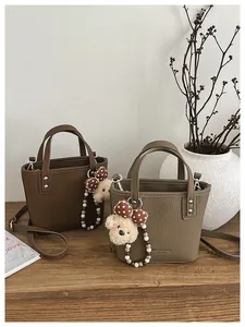 Close-up of litchi grain leather bucket bags with cute bear charms and crossbody straps