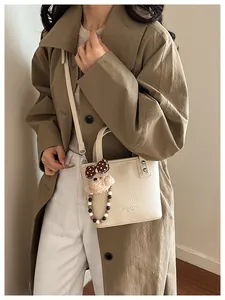 Detail of off-white lychee texture leather bucket bag with cute bear charm and metal rivets