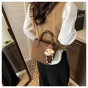 Detail of a brown lychee pattern bucket bag with a cute plush bear charm on a model