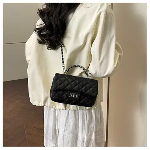Detail of black quilted crossbody bag with silver chain strap and metal handle
