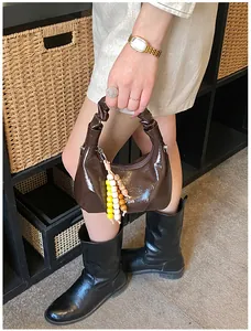 Detail der dunkelbraunen Lackleder-Handtasche mit Faltenhenkel und Perlenanhänger