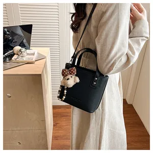 Detail of black lychee grain leather bucket bag with cute plush dog charm on shoulder strap