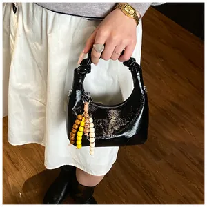 Detail der schwarzen Lackleder-Handtasche mit gerafftem Griff und Perlen-Quaste