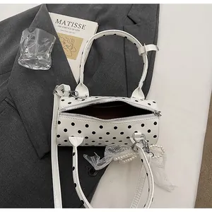 Close-up of polka dot cylinder handbag with pearl charm on a stylish grey blazer background