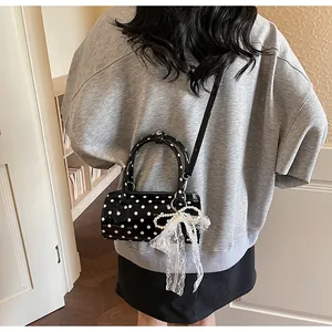 Detail of a black polka dot cylindrical bag with lace bow and pearl charm accent
