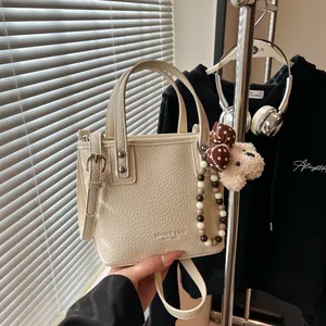 Chic cream textured leather bucket bag with top handles and a cute bear charm