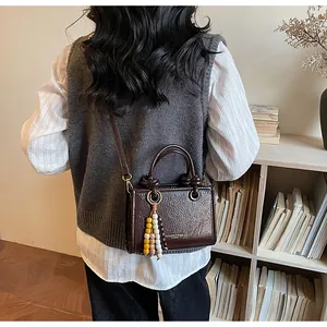 Detail of dark brown glossy wrinkled leather crossbody bag with beaded charm