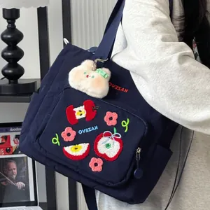 Détail de la broderie pomme et du charm en peluche sur le sac bandoulière en toile bleu marine
