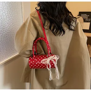 Detail of red polka dot cylinder bag with lace bow and pearl charm on a model