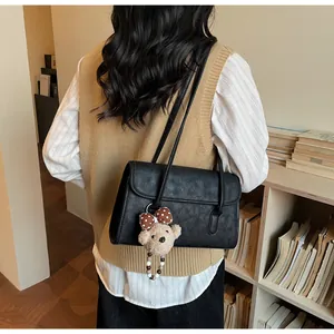 Detail of black faux leather shoulder bag with a cute plush bear pendant and flap closure
