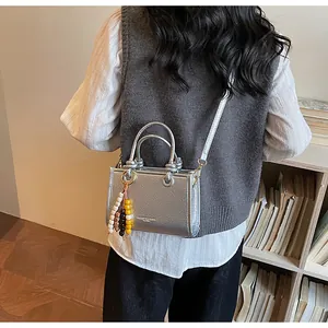 Detail of silver textured mini crossbody bag with round handles and beaded charm accessory