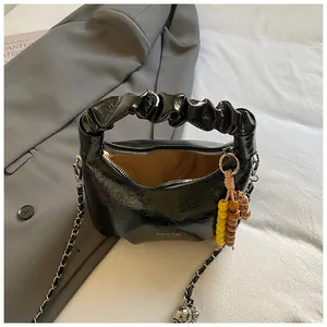 Glänzende schwarze Cloud-Handtasche mit Falten-Griff und Silberkette auf grauem Blazer