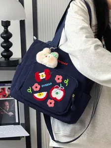 Détail de pomme rouge brodée et motifs floraux sur un sac bandoulière en toile bleu marine