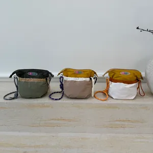 Three Gorpcore nylon crossbody bags with rope straps in various contrast colors on stairs