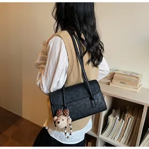 Detail of black vintage shoulder bag with a cute plush bear charm in a retro library setting