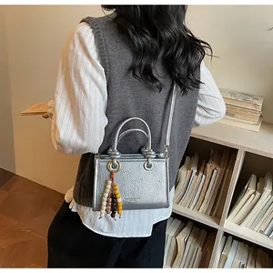 Silver tote bag with pleated texture and colorful beaded tassel shown in a lifestyle setting