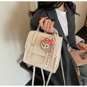 Close-up of cream leather backpack with metal buckles and a cute plush bear charm