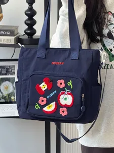 Détails de broderie de pomme et de fleurs sur un sac fourre-tout bleu marine polyvalent