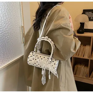 Close-up of white polka dot cylinder bag with lace bow and pearl chain detail
