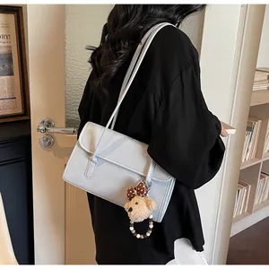 Detail of light blue shoulder bag with a cute plush bear charm on a model's arm