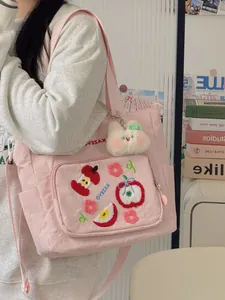 Détail de la broderie de pomme sur un sac cabas en toile rose avec pendentif en peluche