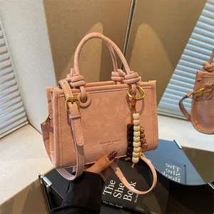 Pink textured leather handbag with beaded charm and adjustable strap in a mirror reflection