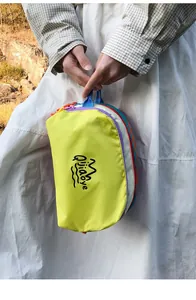 Detail of neon yellow nylon pouch featuring multi-colored zippers and graphic brand logo