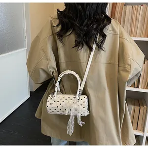 Close-up of white polka dot cylinder bag featuring lace bow and pearl pendant detail