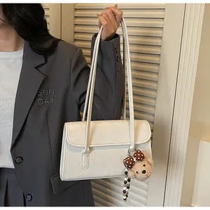 Detail of white minimalist shoulder bag with cute teddy bear charm and flap design