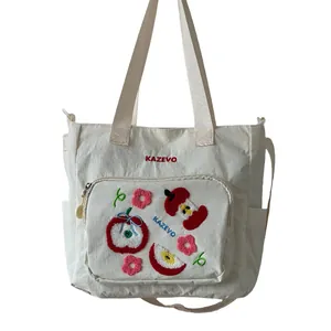 Détail du sac fourre-tout en nylon blanc avec broderie pomme et poche zippée
