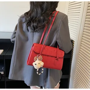 Red shoulder bag with flap design and cute plush bear charm shown on a female model