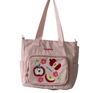 Gros plan détaillé du sac en toile rose avec broderie pomme et poche zippée avant