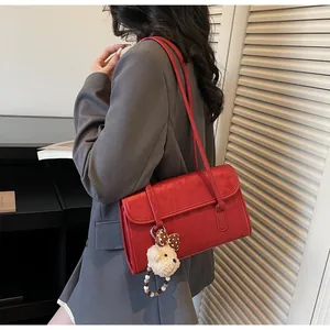 Detail of dark red suede shoulder bag with cute plush bear charm and long straps