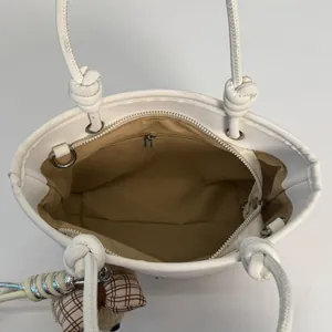 Vue de dessus d'un tote bag blanc avec doublure brune et détail de charm ours
