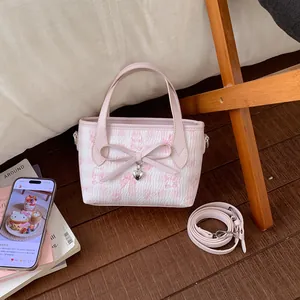Detail of pink bow and heart pendant on printed crossbody bag with detachable strap