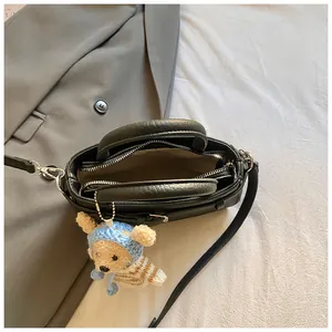 Close-up of black crossbody bag with lychee texture and cute bear charm on a suit