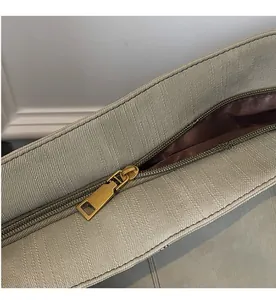 Close-up of smooth golden metal zipper on beige fabric tote bag with dark brown lining