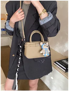 Close-up of khaki small square handbag featuring leather strap buckle and cute teddy bear charm